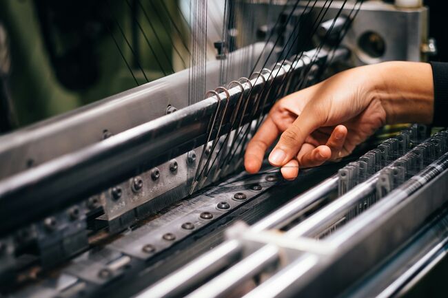 a woman's hand tending to threads in a machine