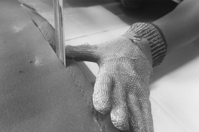 a man with gloves on cuting through fabric with a saw